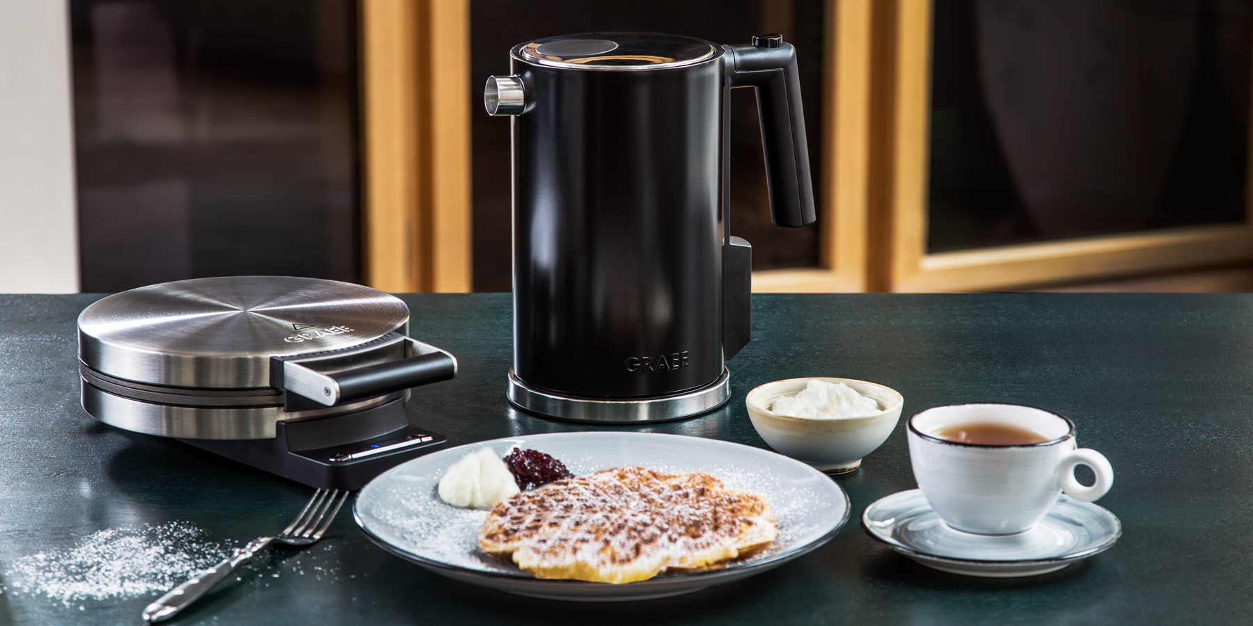 Waffeleisen und ein Wasserkocher von der Marke Greaf auf einer Arbeitsplatte.